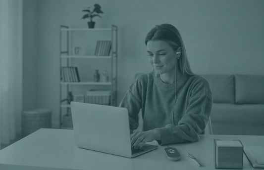 Woman wearing Nurosym device ear piece while working on a laptop at home