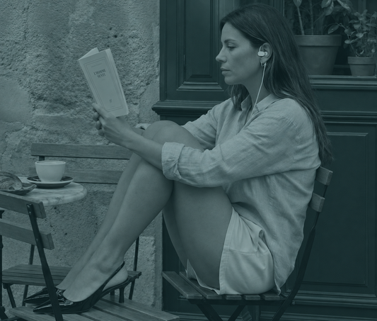 Woman wearing a Nurosym earpiece while reading a book at an outdoor café table