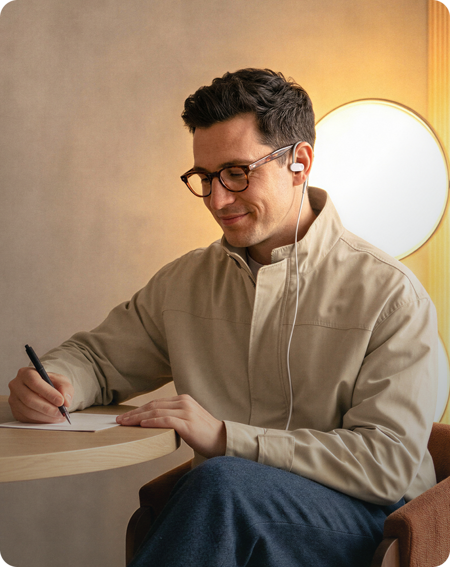 Man writing at a table while wearing Nurosym earbuds