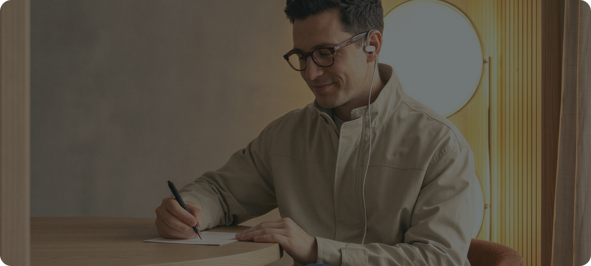 Man writing at a table while wearing Nurosym earbuds